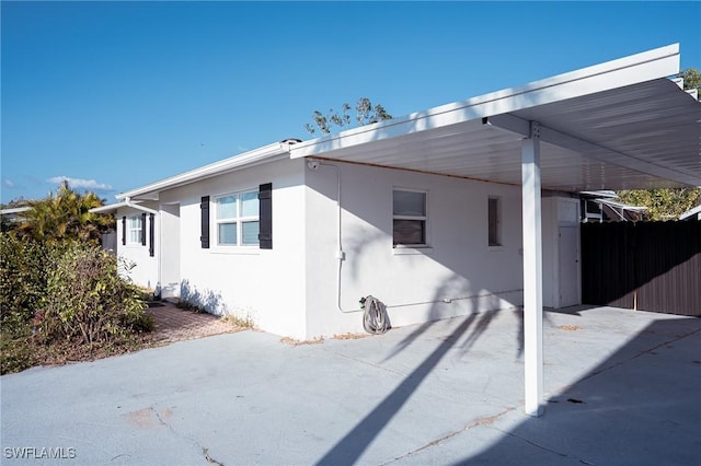 view of side of home with fence, a carport, and stucco siding