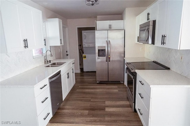 kitchen with dark wood-style flooring, stainless steel appliances, stacked washer / drying machine, decorative backsplash, and a sink