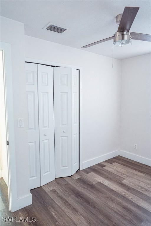 unfurnished bedroom with baseboards, visible vents, ceiling fan, wood finished floors, and a closet