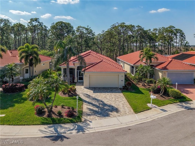 mediterranean / spanish-style house featuring decorative driveway, stucco siding, an attached garage, a front yard, and a tiled roof