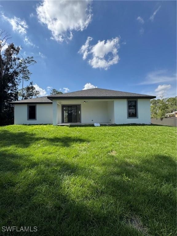 rear view of property with a yard, fence, and stucco siding