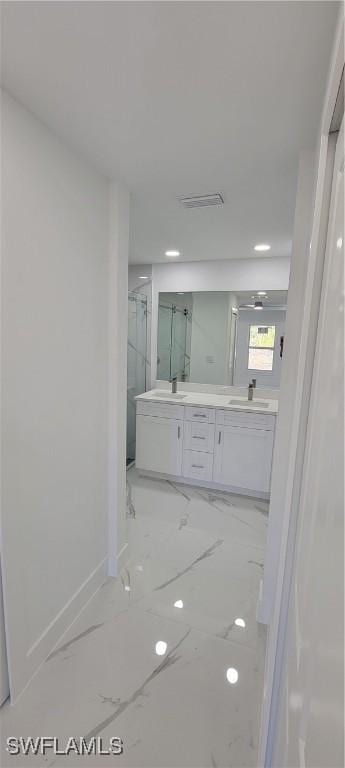 bathroom featuring double vanity, marble finish floor, a marble finish shower, and a sink