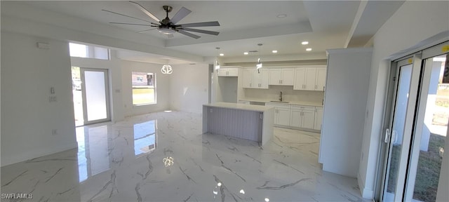 kitchen featuring marble finish floor, a kitchen island, a raised ceiling, and a sink