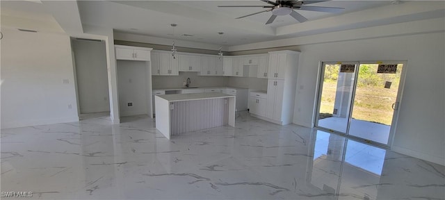 kitchen with a center island, marble finish floor, a tray ceiling, white cabinetry, and a sink