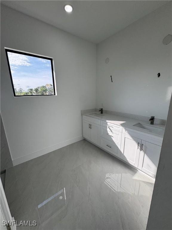 bathroom featuring marble finish floor, double vanity, a sink, and baseboards