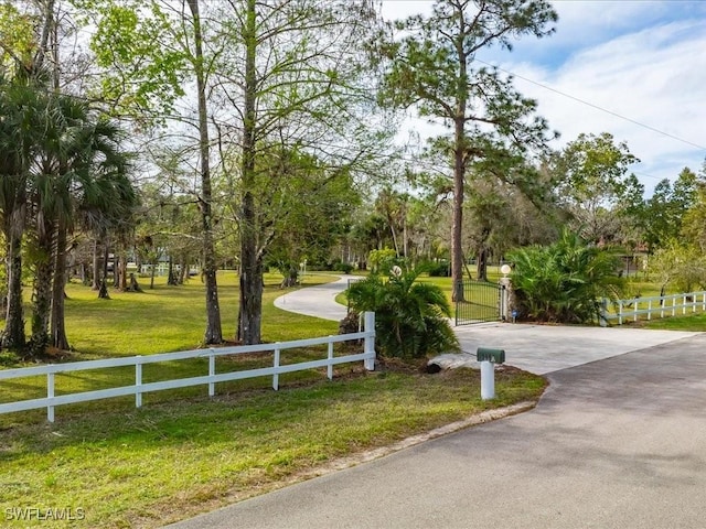 view of home's community featuring aphalt driveway, a gate, a yard, and fence