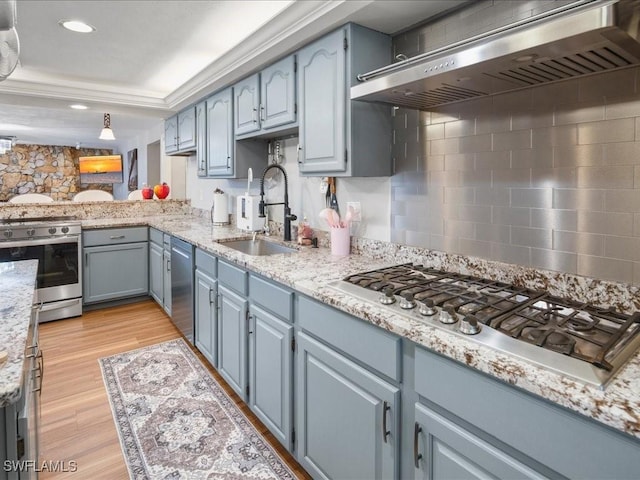 kitchen with a sink, light stone counters, light wood-style floors, appliances with stainless steel finishes, and wall chimney range hood