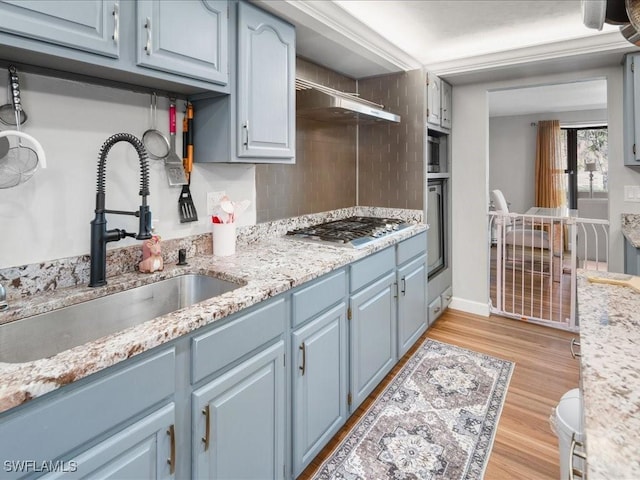 kitchen with tasteful backsplash, under cabinet range hood, light wood-style flooring, stainless steel gas stovetop, and a sink