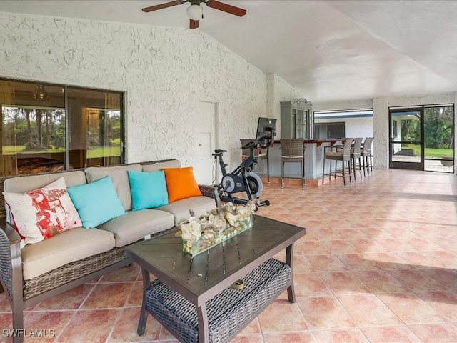 tiled living area featuring ceiling fan, a textured wall, and vaulted ceiling