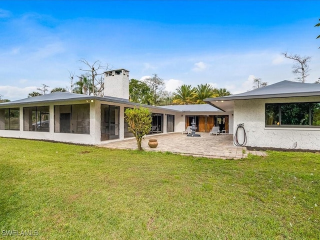 back of house with stucco siding, a lawn, a patio, a sunroom, and a chimney