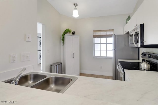 kitchen with stacked washer / dryer, a sink, white cabinetry, baseboards, and appliances with stainless steel finishes