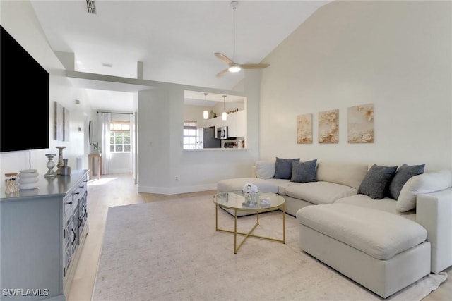 living room featuring ceiling fan, light wood-style flooring, visible vents, baseboards, and vaulted ceiling