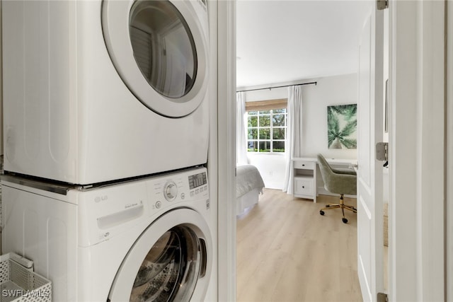 clothes washing area featuring laundry area, light wood finished floors, and stacked washer and clothes dryer