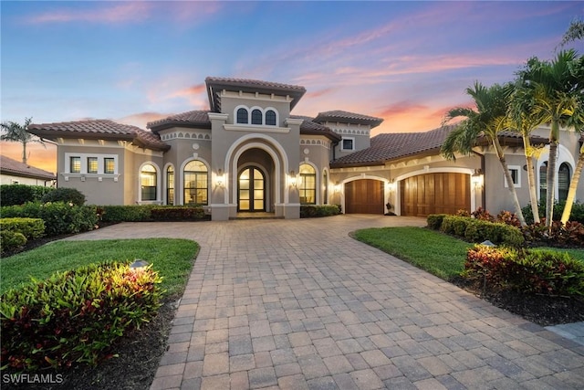 mediterranean / spanish house with a garage, decorative driveway, a tiled roof, and stucco siding