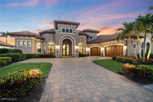mediterranean / spanish-style home featuring a garage, decorative driveway, stucco siding, and a tiled roof