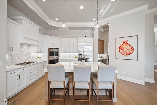 kitchen featuring light wood finished floors, a raised ceiling, light countertops, appliances with stainless steel finishes, and a kitchen breakfast bar