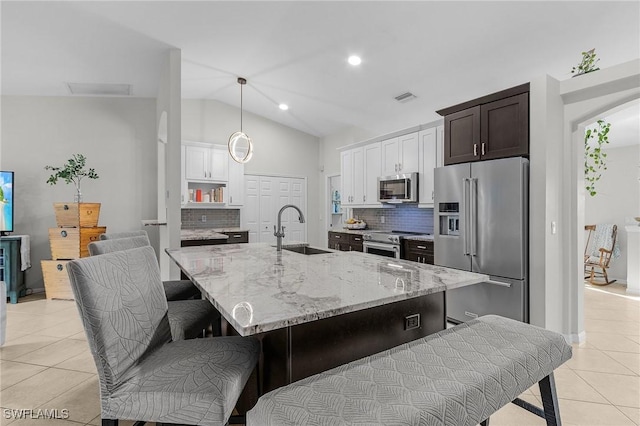 kitchen with light tile patterned floors, stainless steel appliances, a sink, light stone countertops, and tasteful backsplash