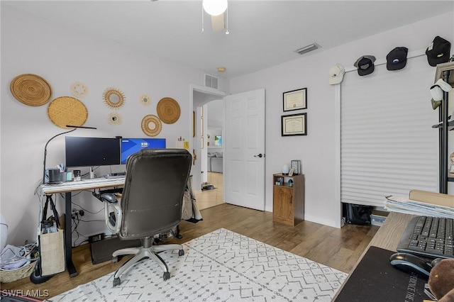 home office with arched walkways, wood finished floors, visible vents, and baseboards