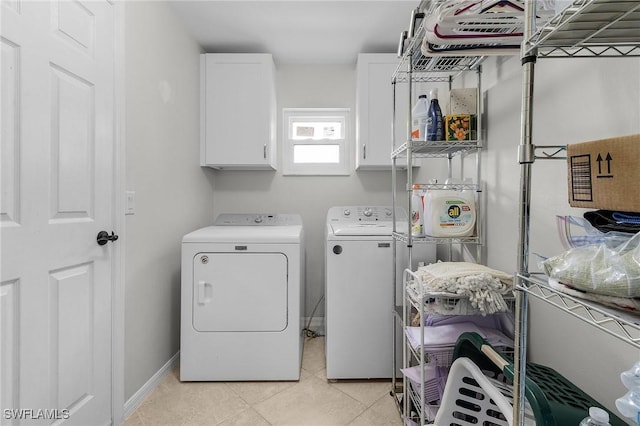 clothes washing area with light tile patterned floors, washing machine and clothes dryer, cabinet space, and baseboards