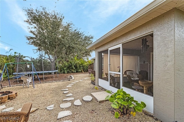 view of yard featuring a trampoline, a sunroom, and a fire pit