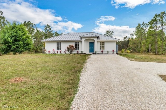 ranch-style home featuring stucco siding, a standing seam roof, metal roof, driveway, and a front lawn