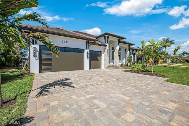 view of front of property featuring stucco siding, decorative driveway, a front lawn, and an attached garage