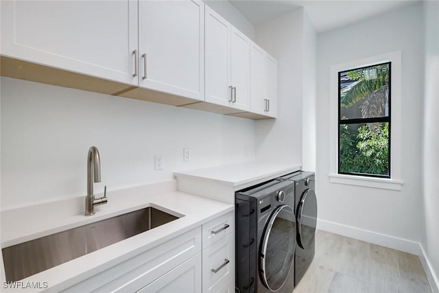 laundry area featuring baseboards, washing machine and clothes dryer, cabinet space, a sink, and light wood-type flooring