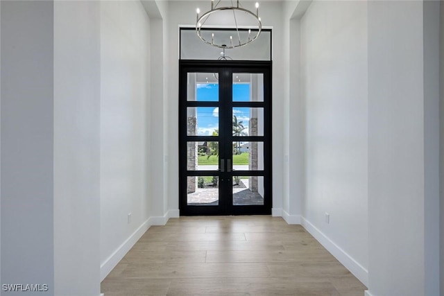 foyer entrance featuring french doors, baseboards, an inviting chandelier, and light wood-style flooring