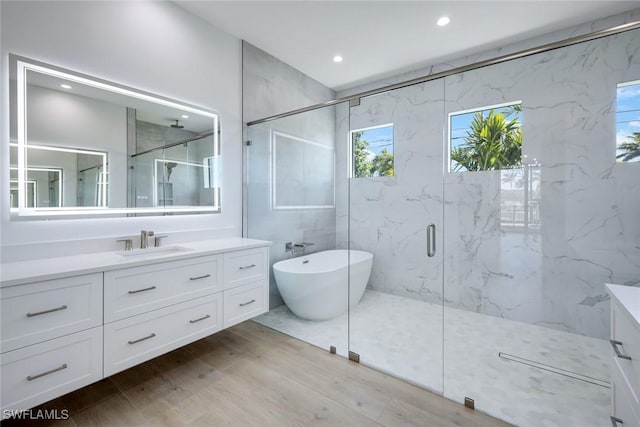 full bathroom featuring wood finished floors, recessed lighting, a marble finish shower, a soaking tub, and vanity