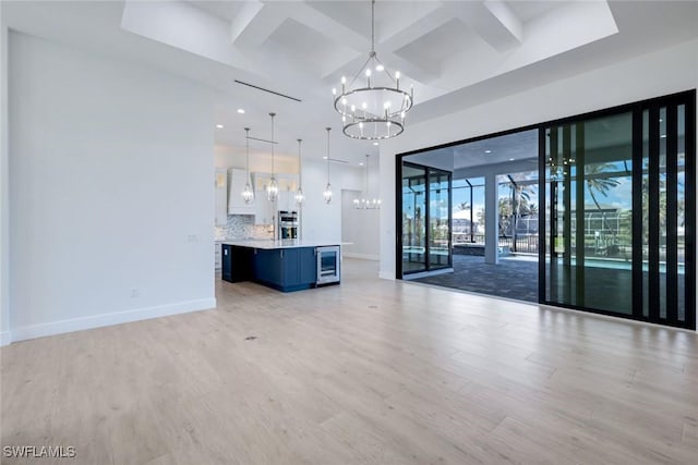 unfurnished living room featuring baseboards, light wood finished floors, coffered ceiling, wine cooler, and a notable chandelier