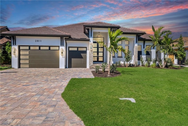 view of front of home with decorative driveway, a front lawn, an attached garage, and stucco siding