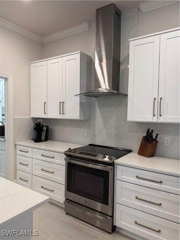 kitchen with tasteful backsplash, white cabinets, stainless steel electric range oven, crown molding, and wall chimney range hood