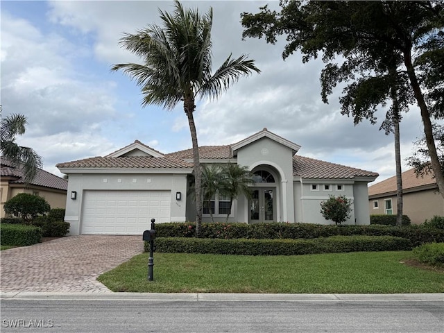 mediterranean / spanish-style home with decorative driveway, a front yard, an attached garage, and stucco siding