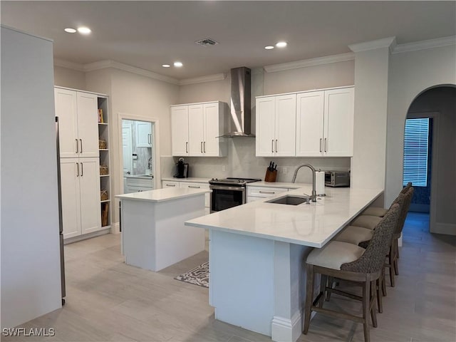 kitchen with arched walkways, wall chimney exhaust hood, a peninsula, stainless steel electric range, and a sink