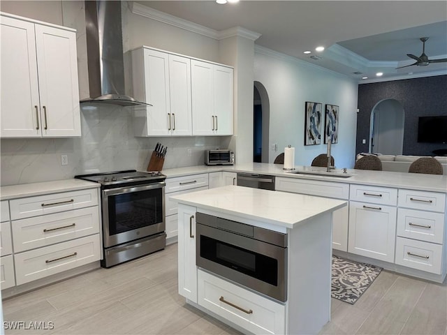 kitchen featuring backsplash, appliances with stainless steel finishes, open floor plan, wall chimney range hood, and a peninsula