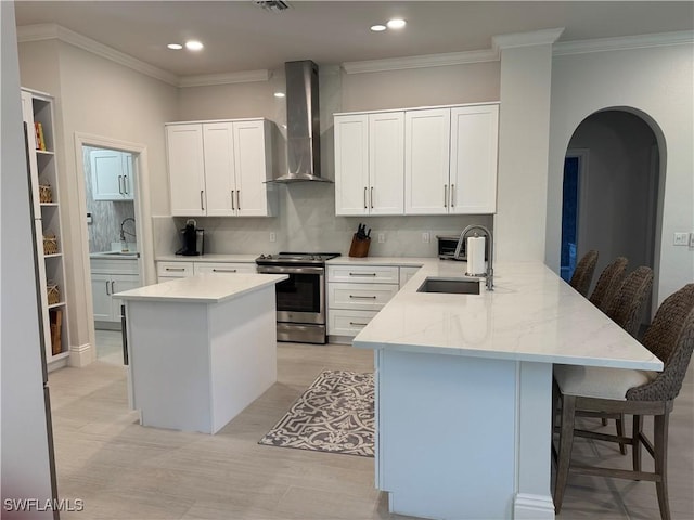 kitchen featuring arched walkways, wall chimney exhaust hood, a peninsula, stainless steel range with electric stovetop, and a sink