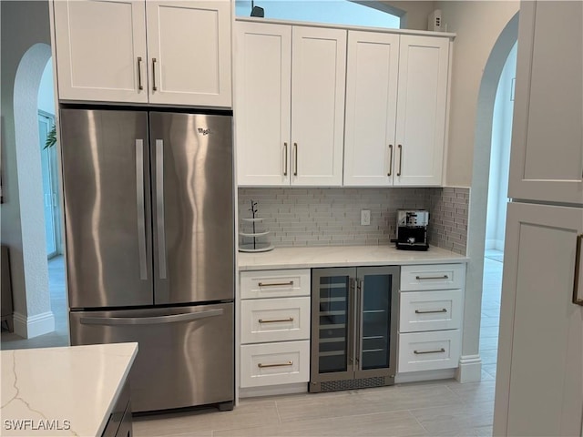 kitchen featuring beverage cooler, arched walkways, white cabinets, decorative backsplash, and freestanding refrigerator