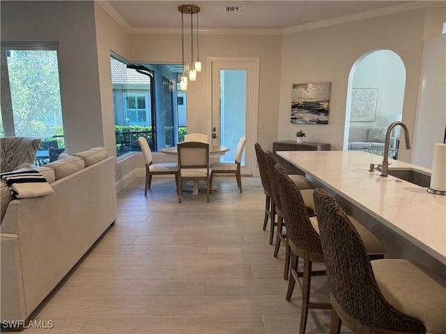 dining space with visible vents, arched walkways, baseboards, ornamental molding, and light wood-type flooring