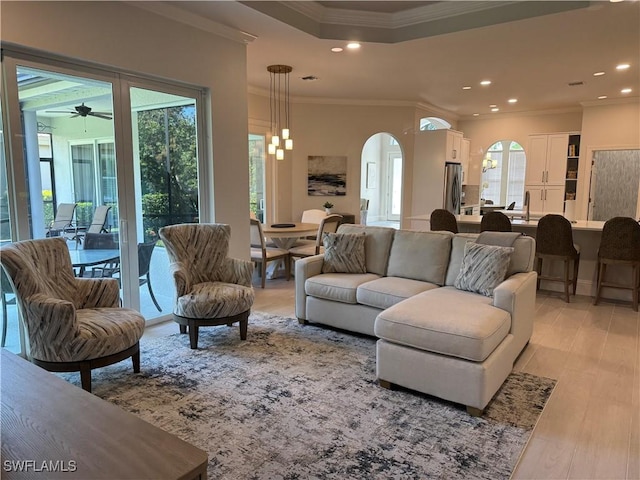 living area featuring light wood-type flooring, crown molding, arched walkways, and recessed lighting