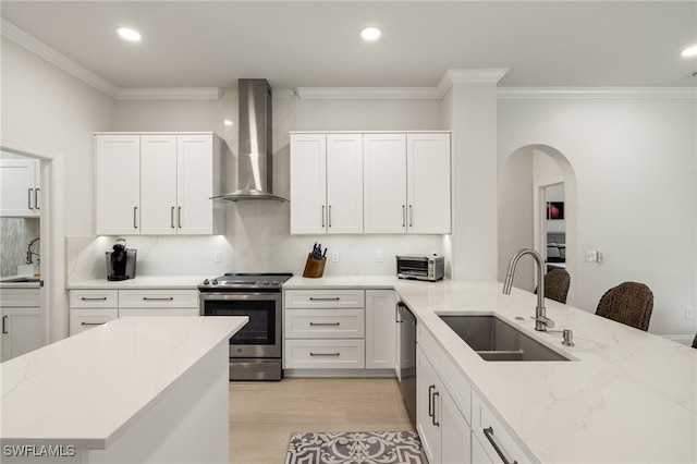 kitchen with arched walkways, stainless steel electric range, wall chimney range hood, and a sink