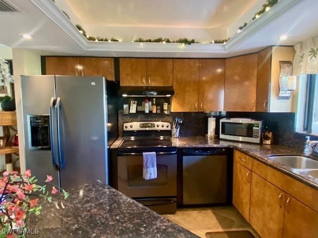 kitchen with brown cabinets, decorative backsplash, appliances with stainless steel finishes, dark stone counters, and under cabinet range hood