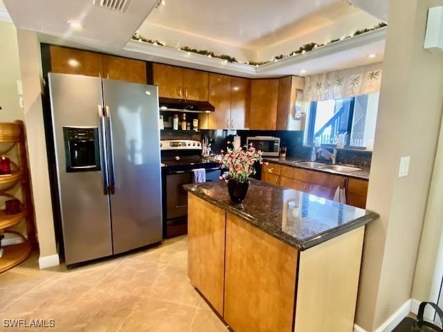 kitchen featuring light tile patterned floors, under cabinet range hood, stainless steel appliances, a sink, and brown cabinets