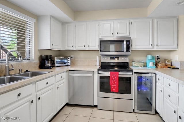 kitchen with light tile patterned floors, beverage cooler, a sink, white cabinets, and appliances with stainless steel finishes