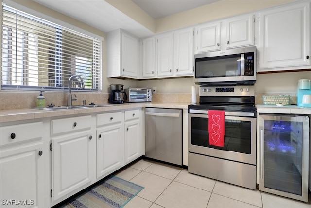 kitchen with beverage cooler, a sink, white cabinets, light countertops, and appliances with stainless steel finishes