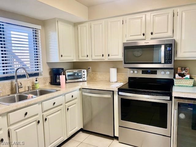 kitchen featuring beverage cooler, a sink, white cabinets, light countertops, and appliances with stainless steel finishes