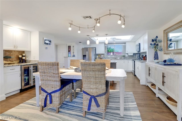 dining space featuring beverage cooler, a skylight, wood finished floors, and visible vents