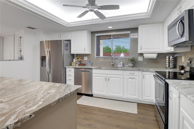 kitchen featuring stainless steel appliances, dark wood-style flooring, white cabinets, backsplash, and a tray ceiling