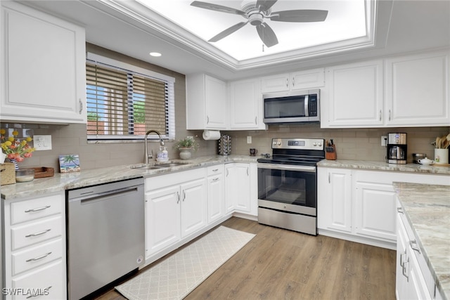 kitchen featuring a raised ceiling, light wood-style flooring, appliances with stainless steel finishes, white cabinetry, and a sink