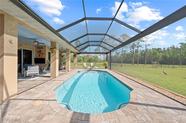 outdoor pool with ceiling fan, glass enclosure, a patio, and a lawn