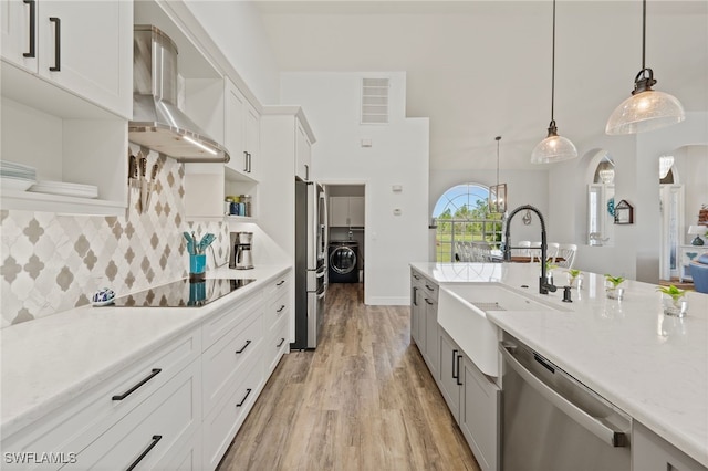 kitchen featuring open shelves, appliances with stainless steel finishes, a sink, wall chimney range hood, and washer and dryer